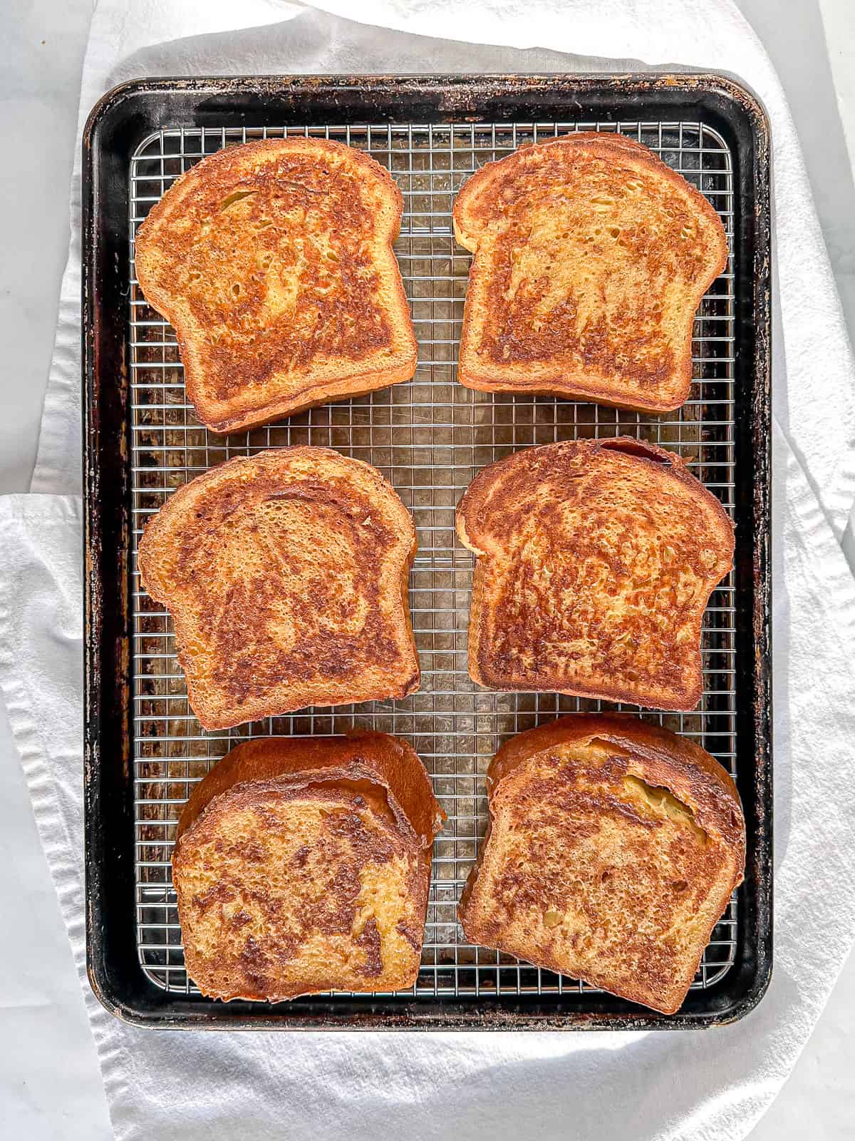 Six slices of eggnog French toast on a wire, wrapped placed in a large sheet pan.