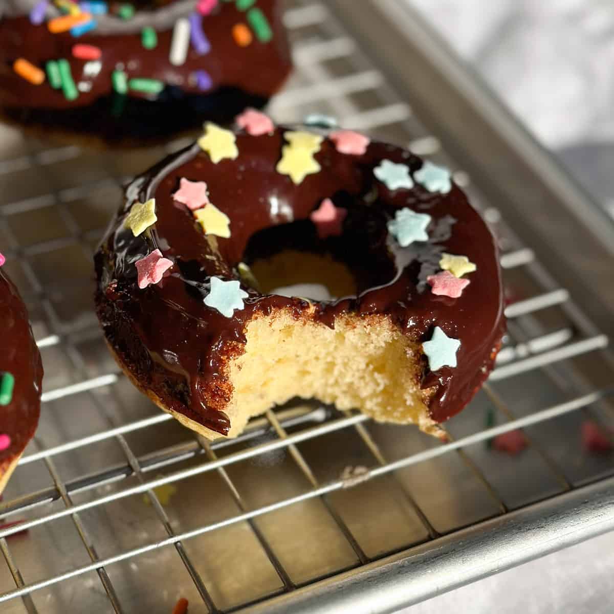 Baked chocolate glaze donuts on a wire rack, one with a bite taken out.
