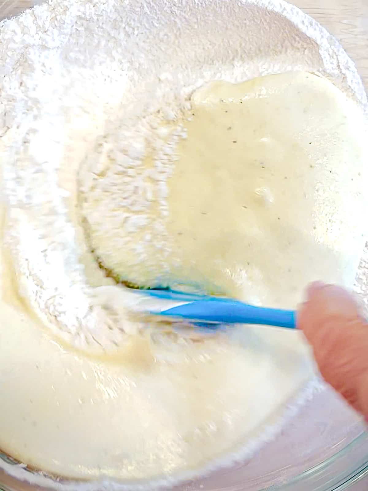 Mixing together wet ingredients with try ingredients to make vanilla donuts.