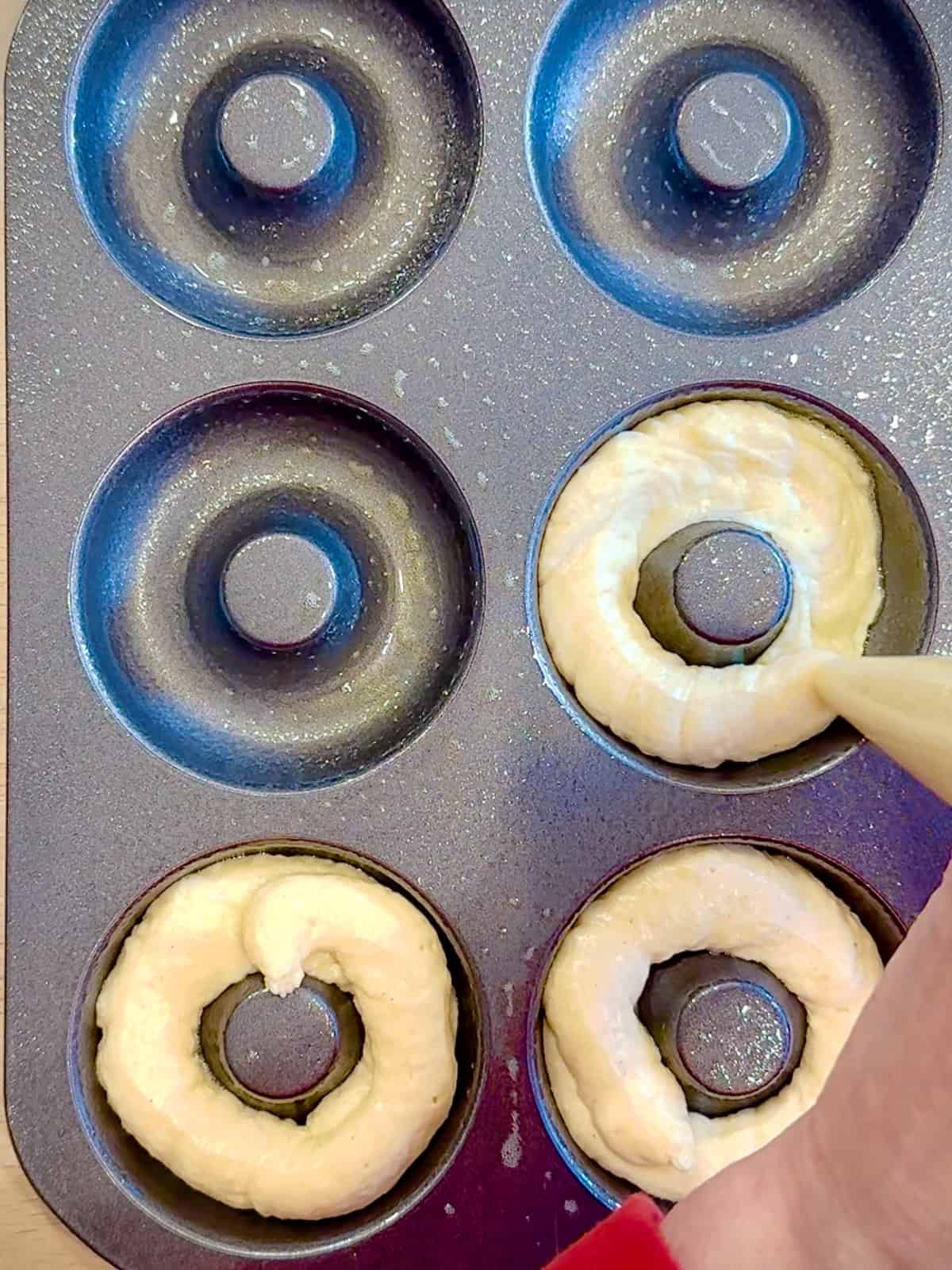 Piping vanilla donut batter into a donut pan.