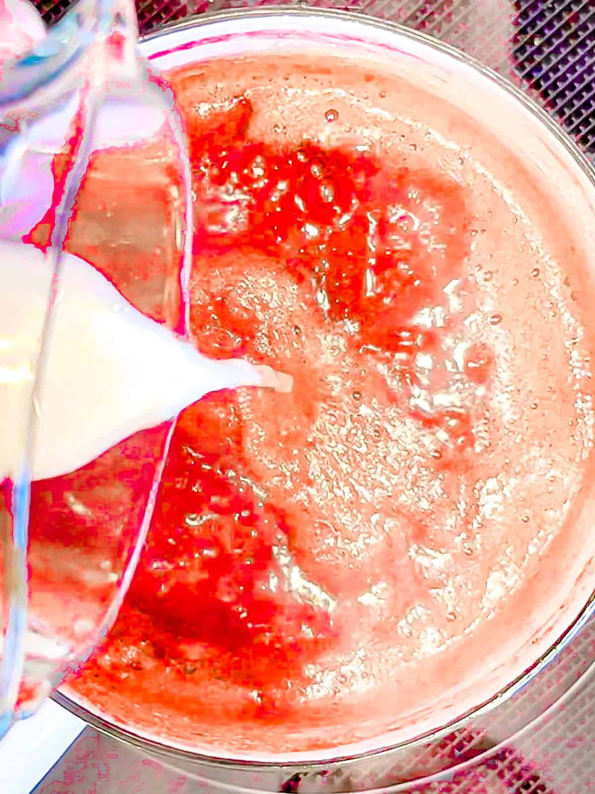 Adding a corn starch slurry to strawberry sauce.
