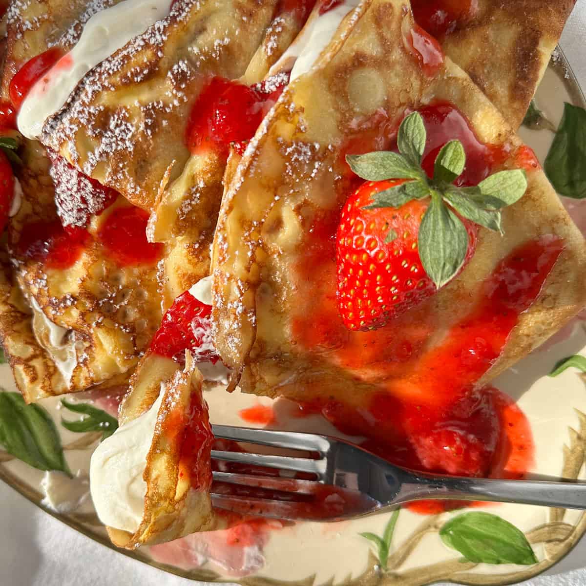 Strawberry crêpes with whipped Greek yogurt, cream, and strawberry sauce on a flowered platter.
