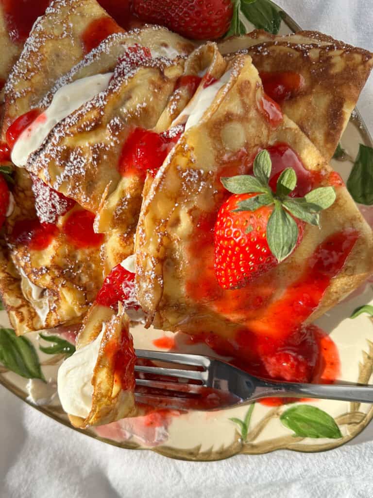 Strawberry crêpes with whipped Greek yogurt, cream, and strawberry sauce on a flowered platter.
