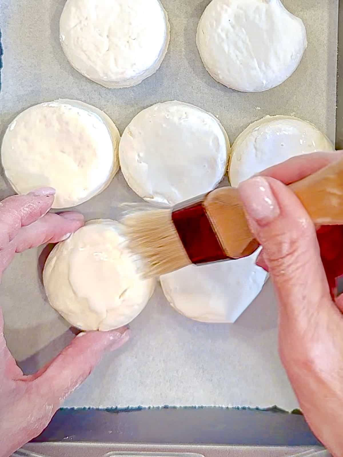 Brushing heavy cream on top of cut out biscuits.