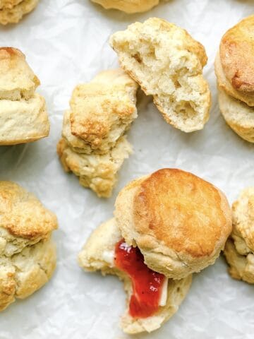 Two ingredient biscuits on parchment paper, one split open with strawberry jam.