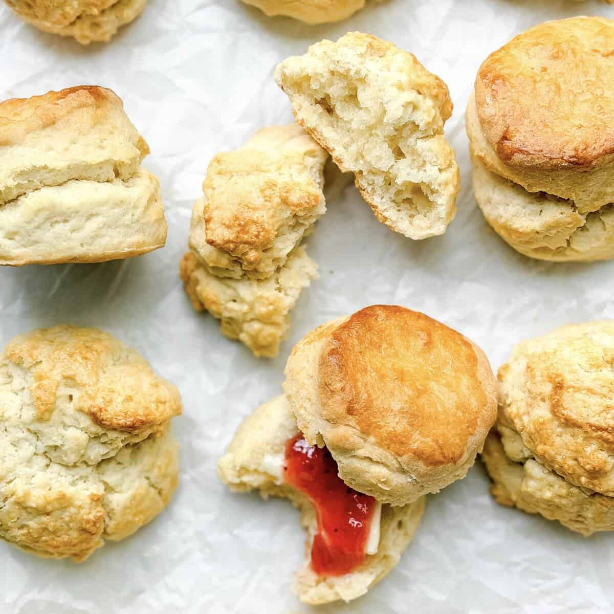 Two ingredient biscuits on parchment paper, one split open with strawberry jam.