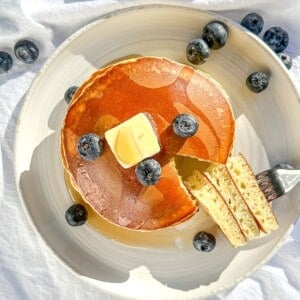 Three ingredient pancakes on a white plate with butter and syrup and fruit.