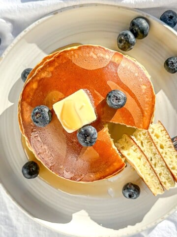 Three ingredient pancakes on a white plate with butter and syrup and fruit.