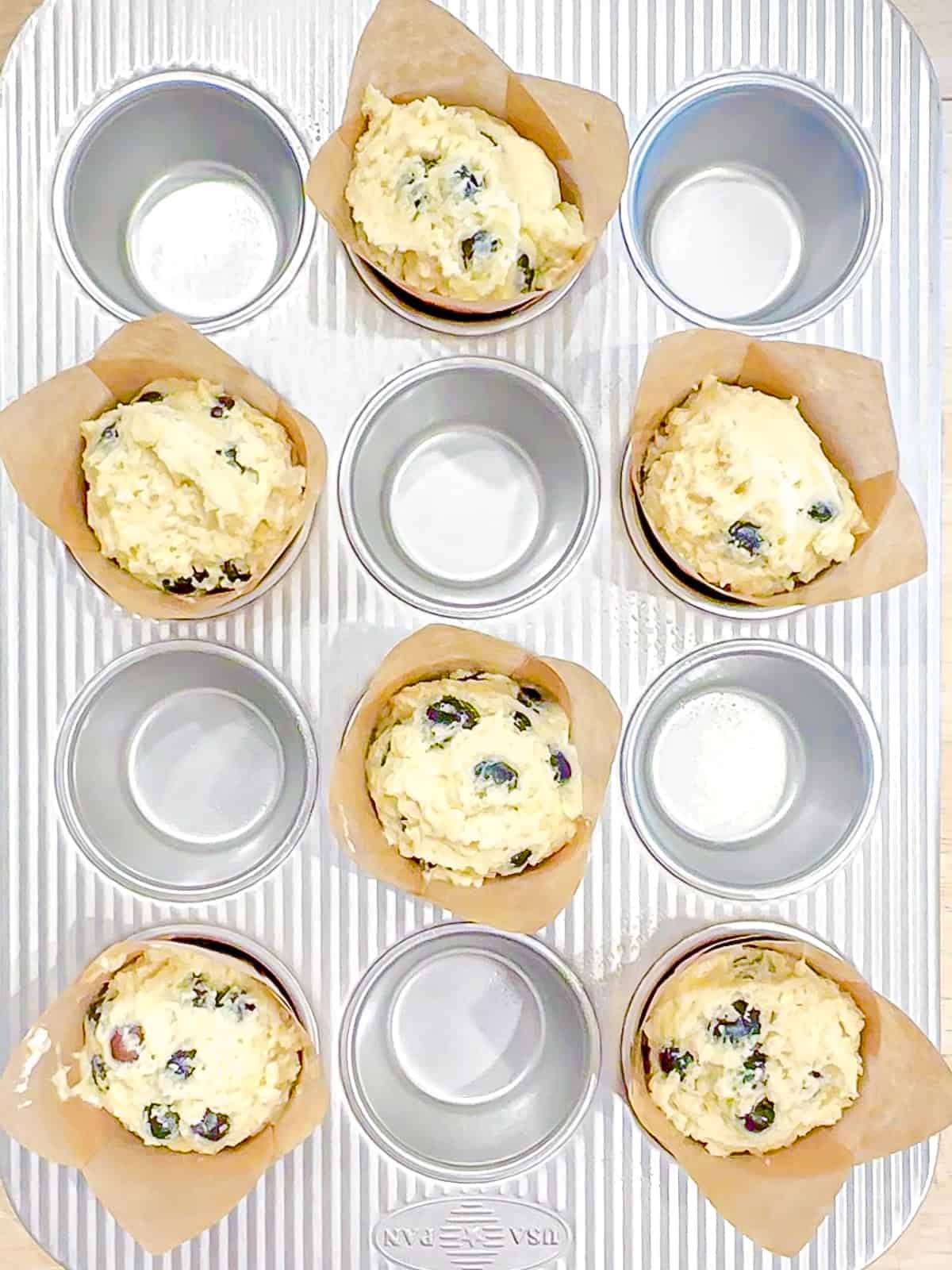 Blueberry muffin batter scooped into muffin liners.