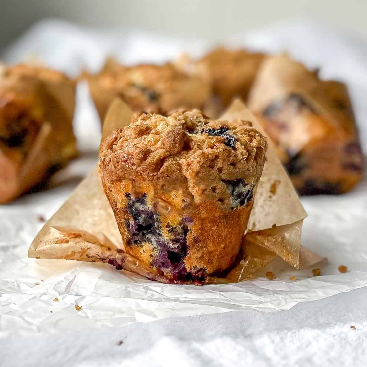 Exterior of a bakery style blueberry streusel muffin with the muffin liner peeled back.
