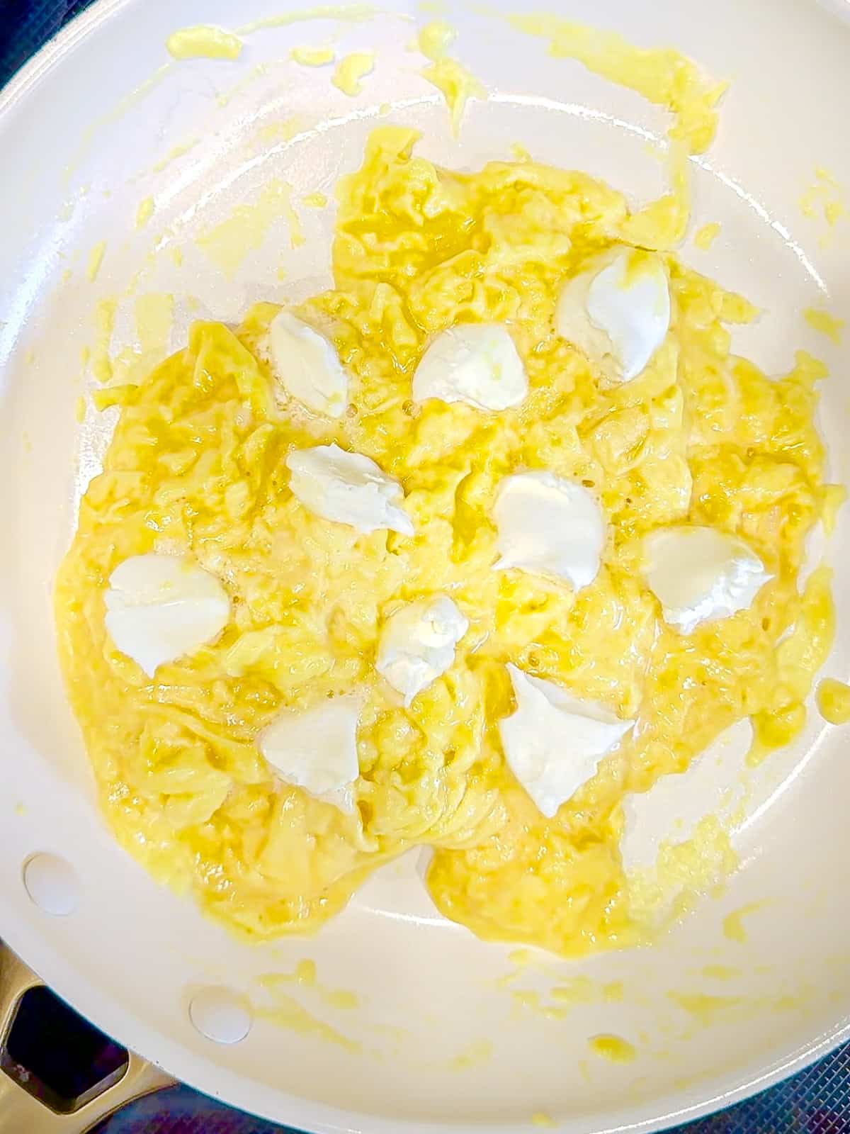 Scrambled eggs in a pan with dollops of mascarpone cheese on top.