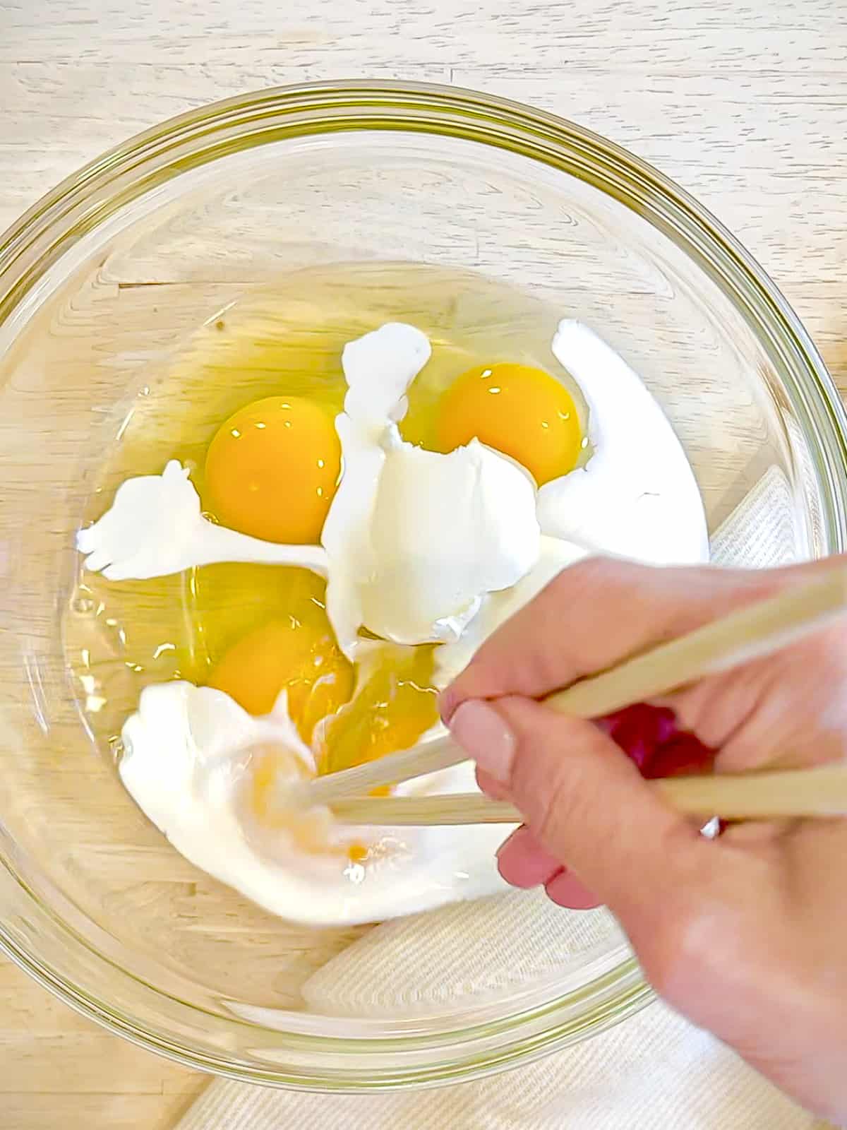 Whisking eggs, mascarpone, cheese, and heavy cream in a bowl.