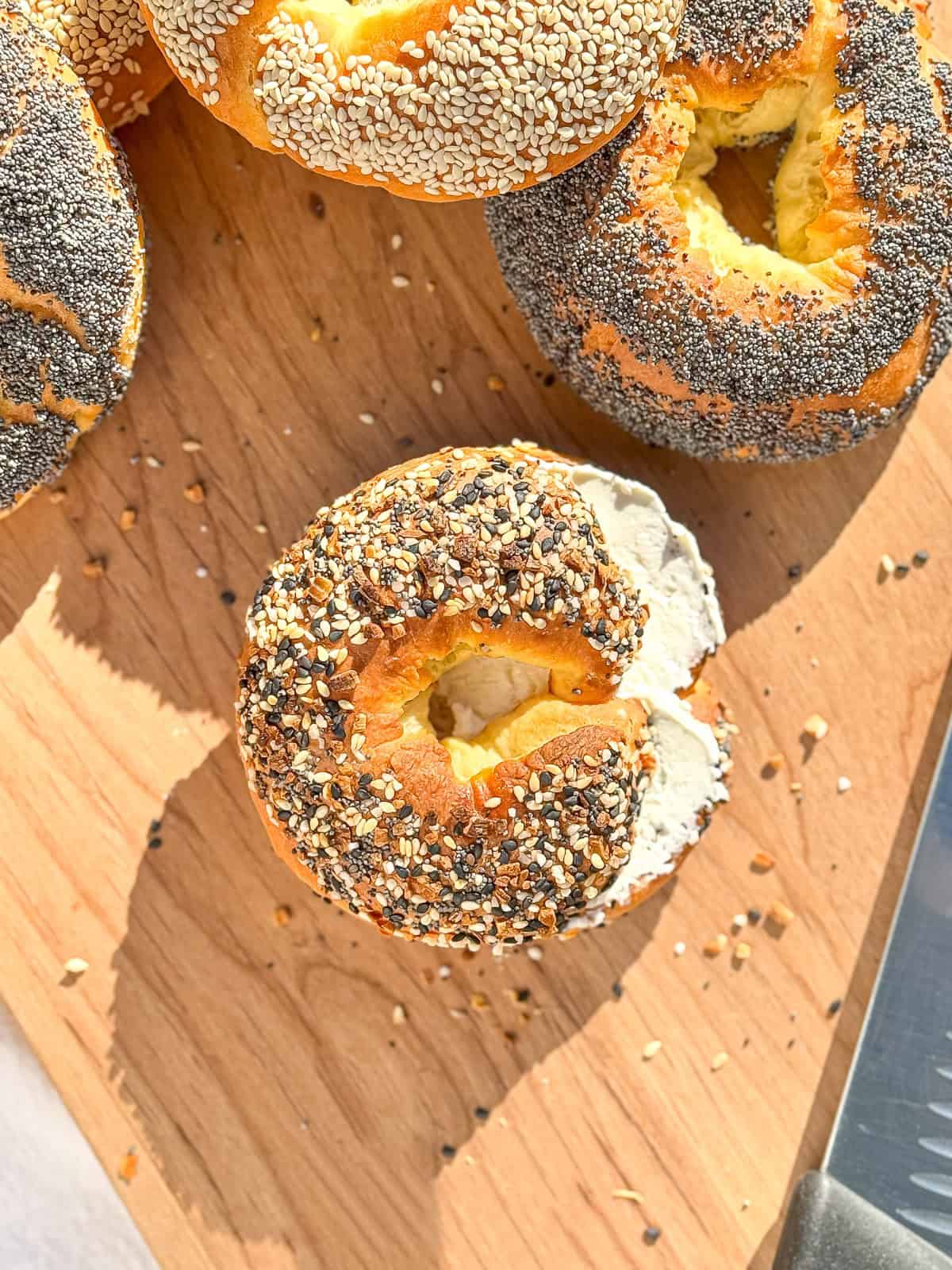 Two ingredient bagels, one with cream cheese, on a wooden cutting board.