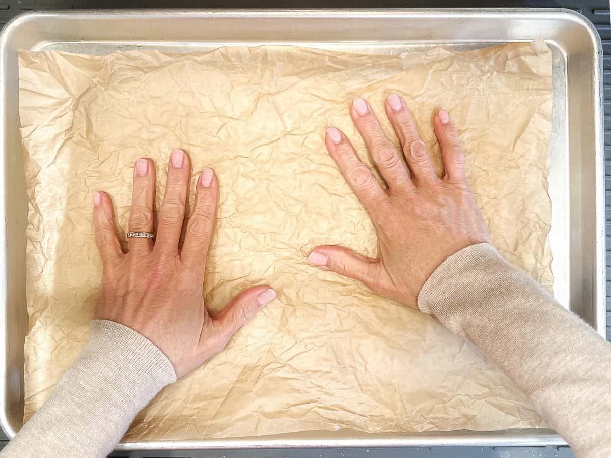 Using hand to smooth out parchment paper on a sheet pan.