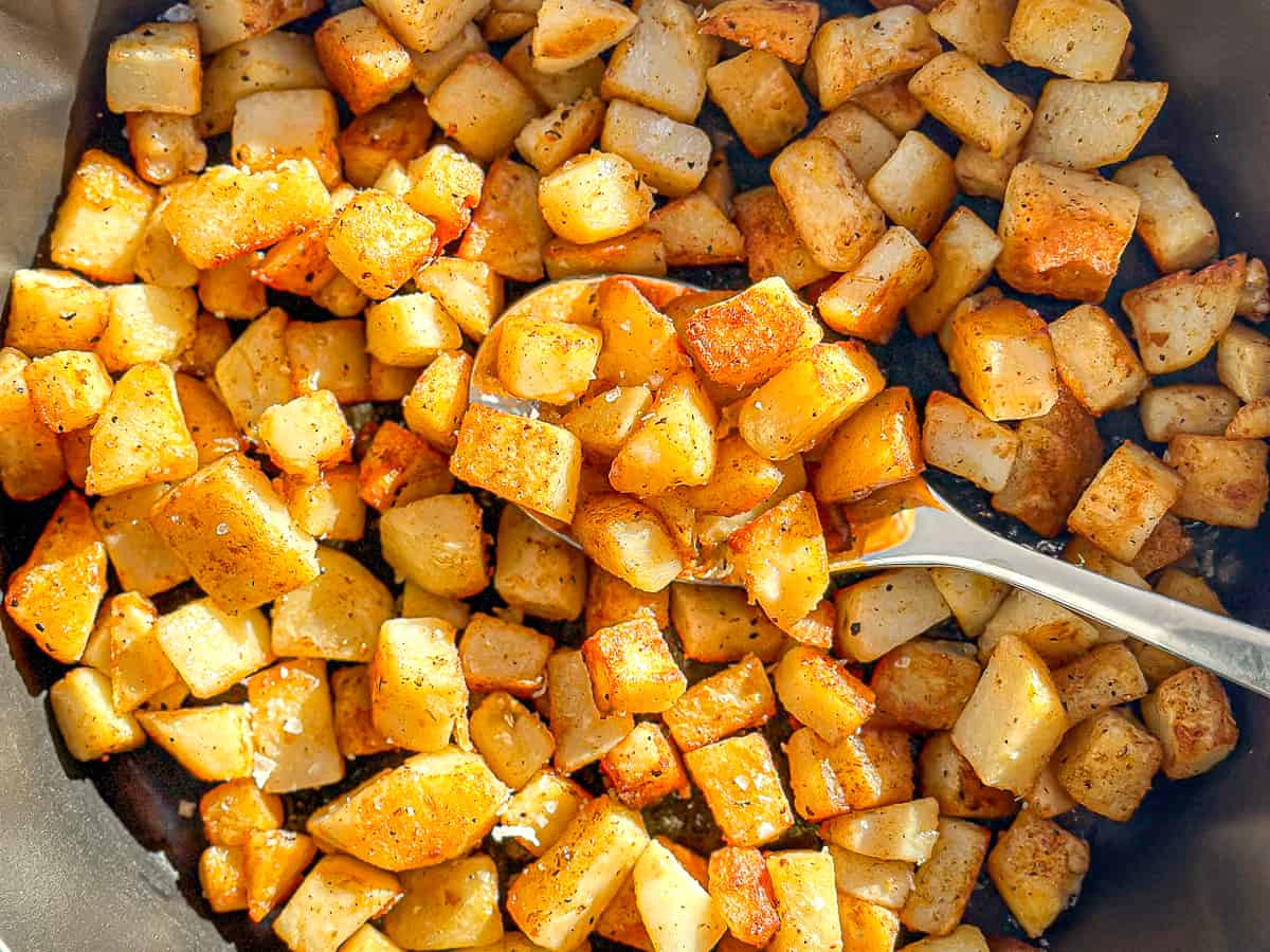 A skillet full of crispy potatoes with a spoon.