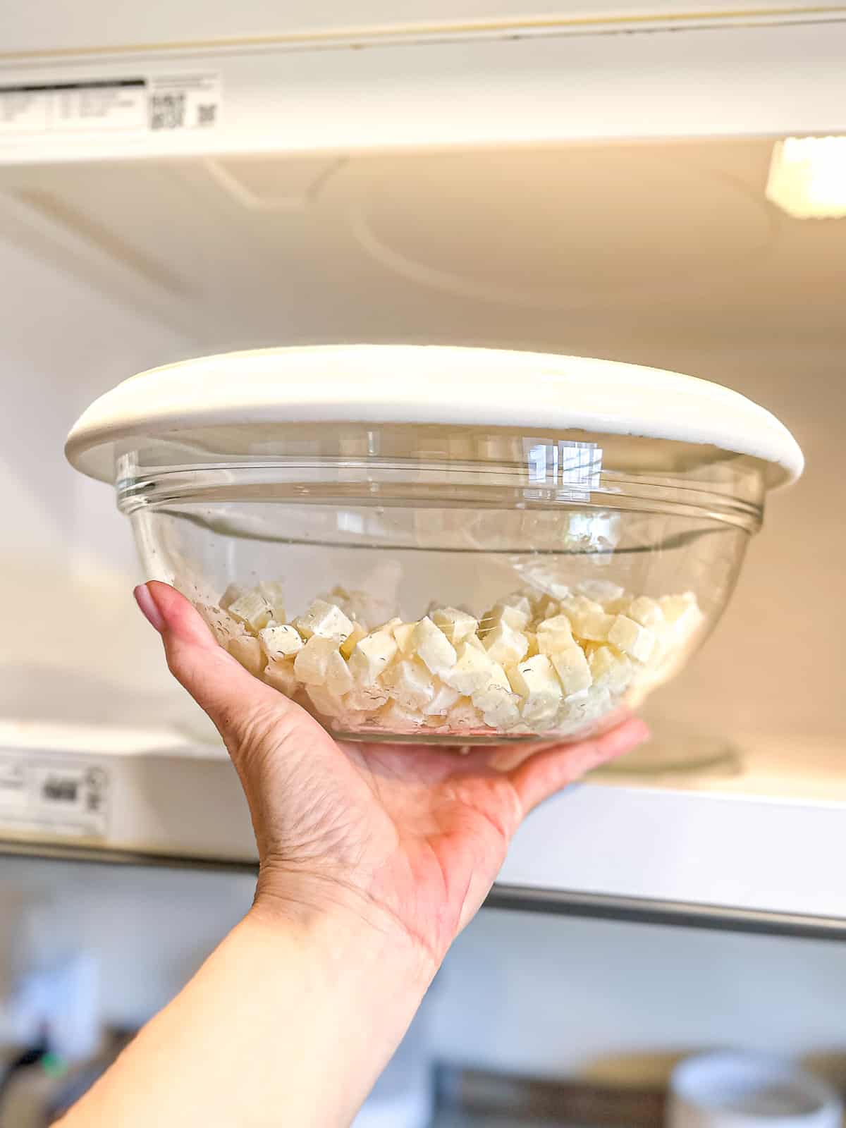 Potatoes in a glass bowl with a plate, turned over top being put into a microwave.