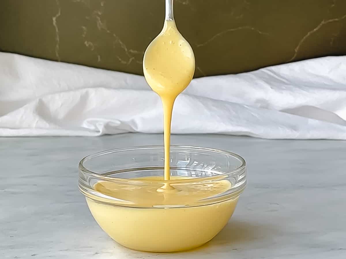 A spoon dripping easy blender hollandaise sauce into a bowl.