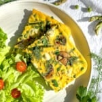 Slices of spring asparagus frittata on a plate with a side salad.
