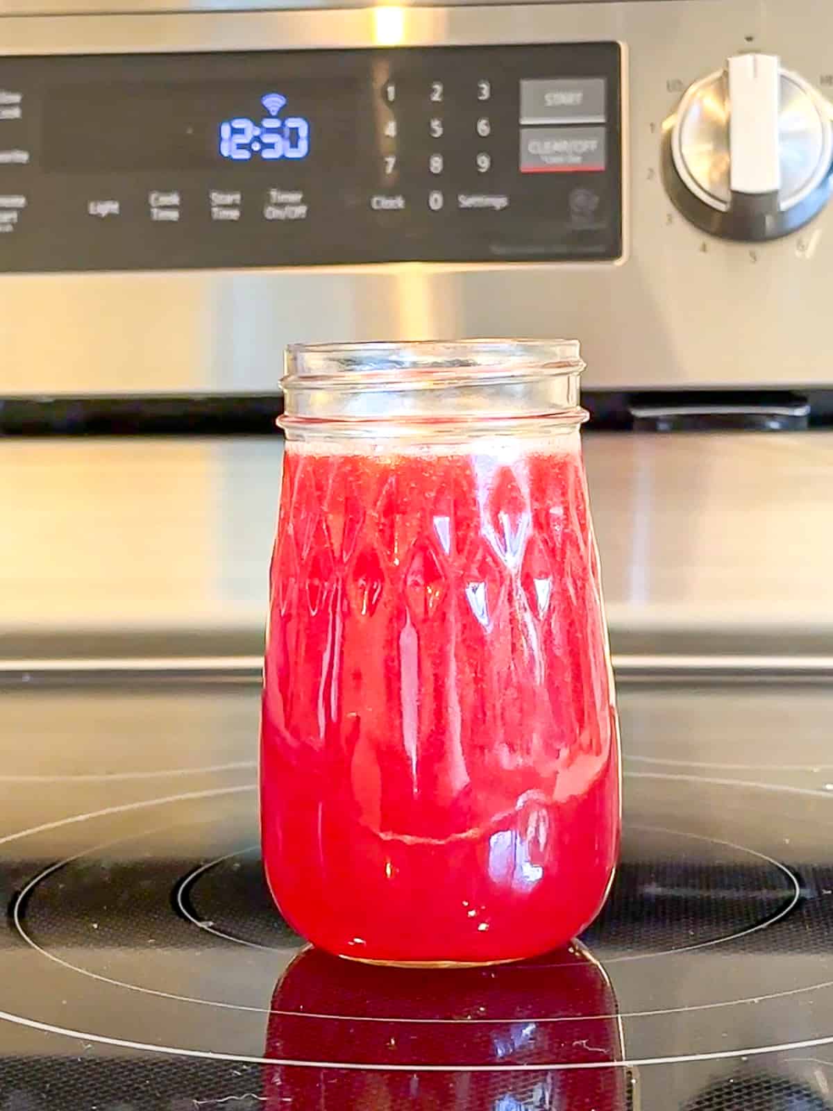 A mason jar of strawberry simple syrup on the stove.