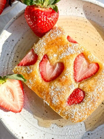 Strawberry sheet pan pancake on a white plate with syrup and fresh berries.