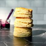 A stack of large biscuits on the black counter against a white tile wall.