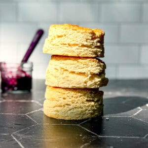 A stack of large biscuits on the black counter against a white tile wall.