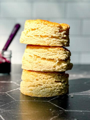 A stack of large biscuits on the black counter against a white tile wall.