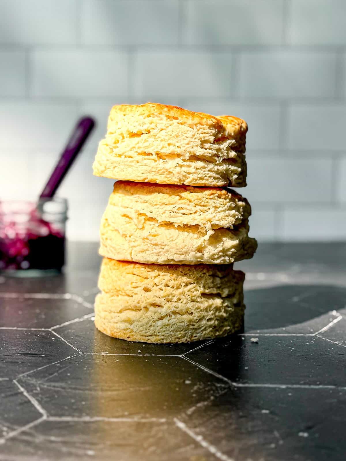 A stack of large biscuits on the black counter against a white tile wall.