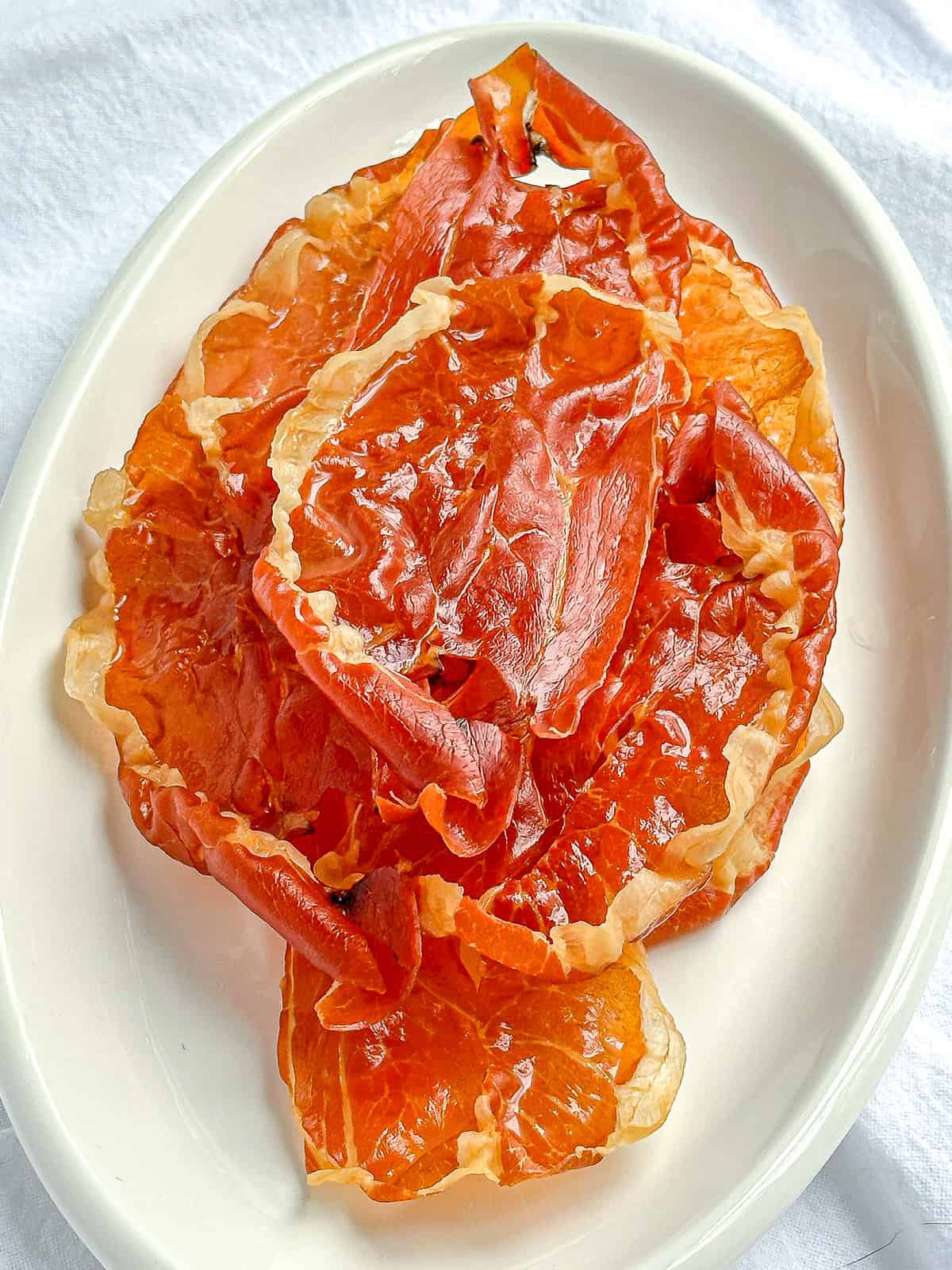 Oval white platter with pieces of crispy prosciutto.