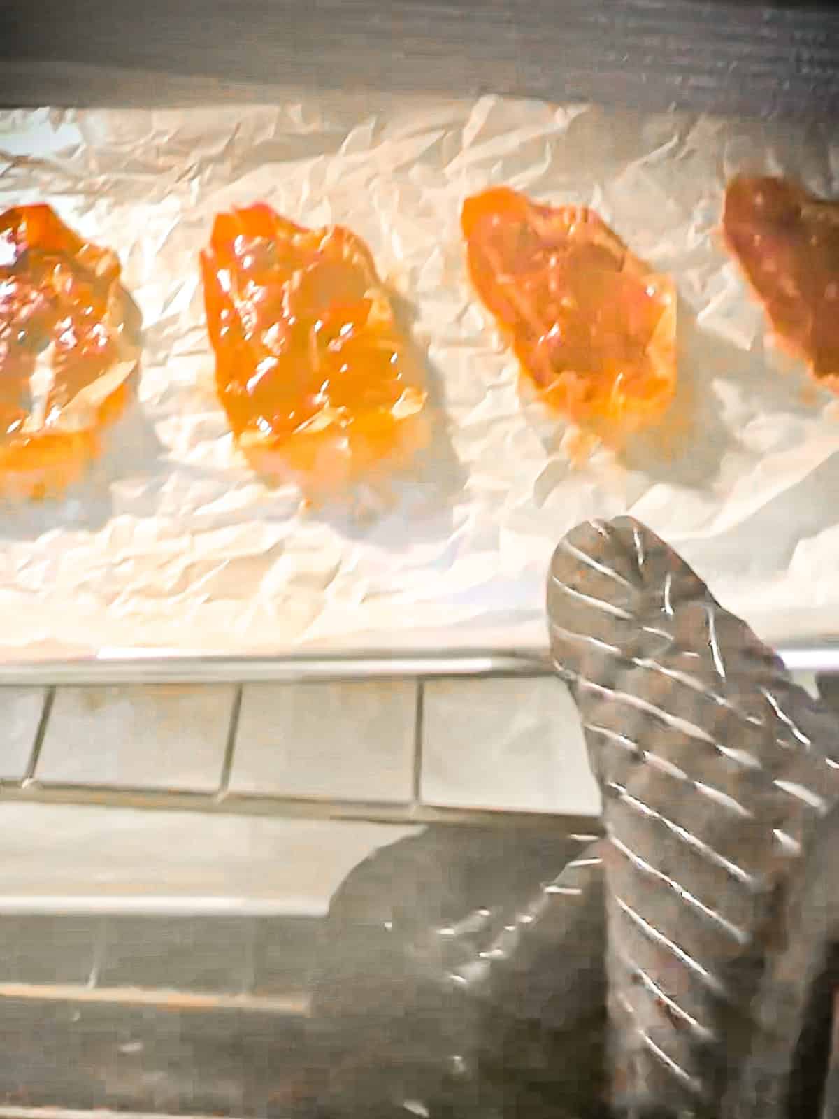 Removing a tray of half cooked prosciutto from the oven to switch oven racks with the second tray.