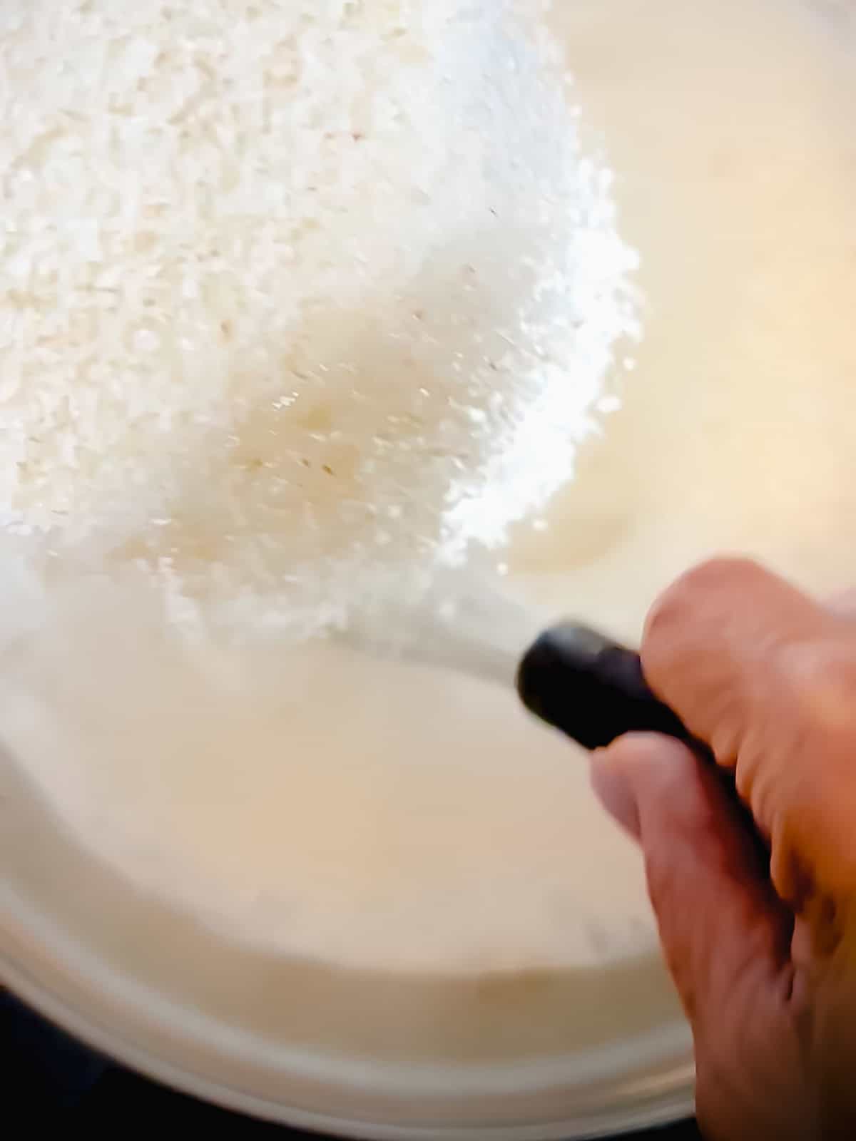 Whisking milk and broth in a saucepan as grits are streamed in.