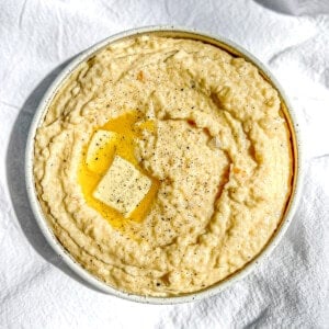 Angled view of a bowl of creamy cheese grits with melting butter on top.