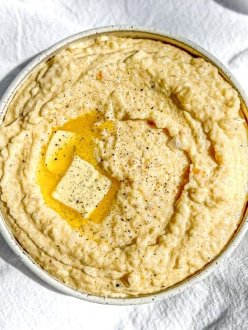 Angled view of a bowl of creamy cheese grits with melting butter on top.