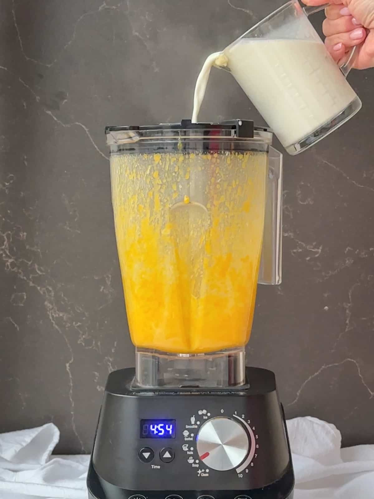 Pouring vanilla, cream, and milk mixture into egg yolks and sugar in a blender.