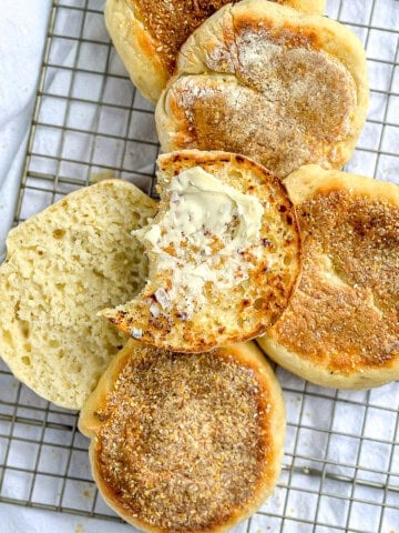Quick and easy English muffins on a wire rack, one smeared with butter.