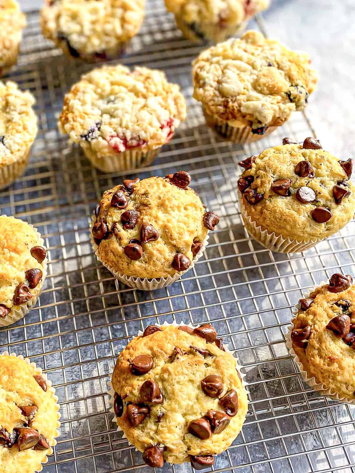 Fruit streusel muffins and chocolate chip muffins on a wire rack.