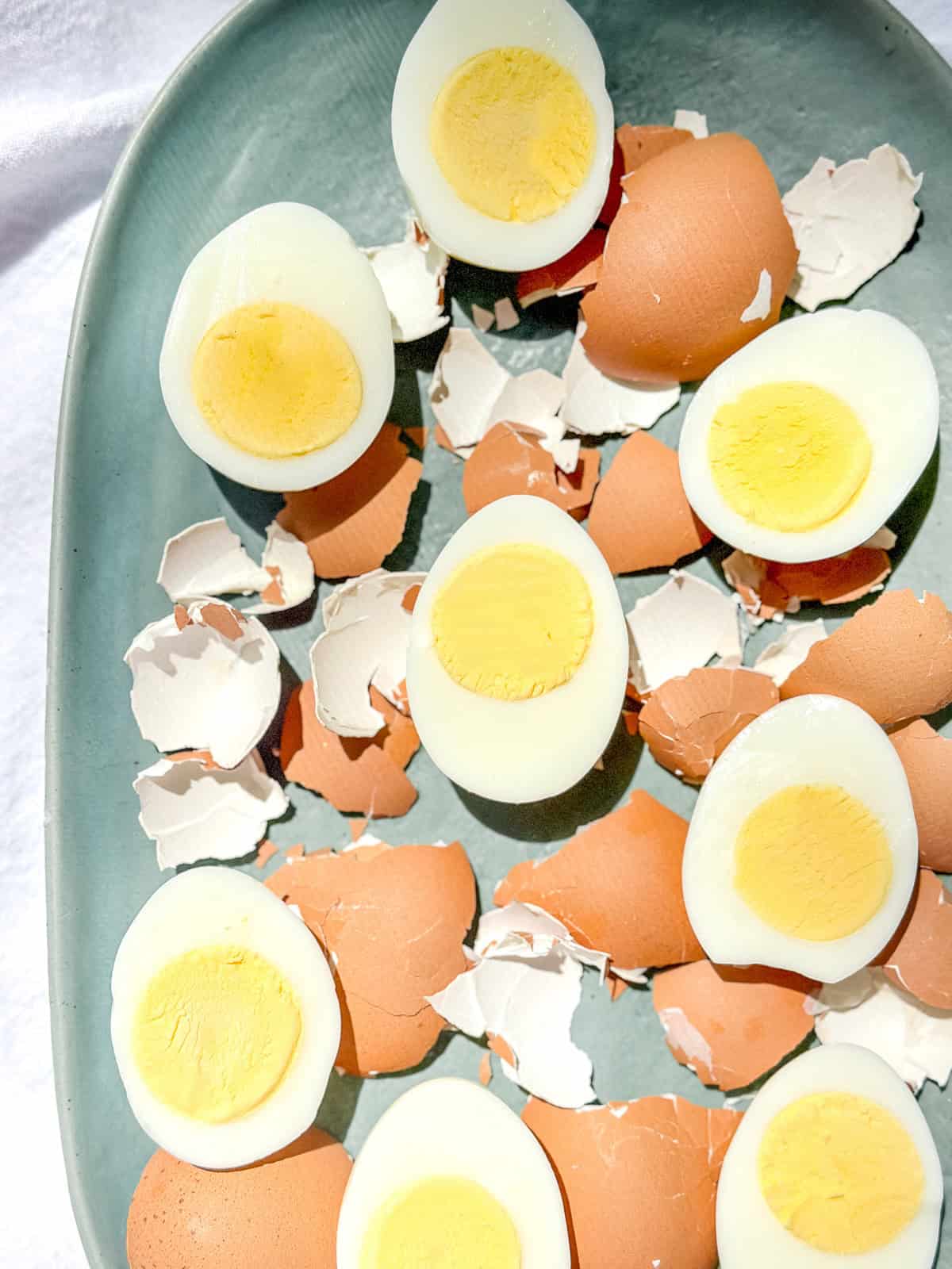 Sliced boiled eggs on green platter with egg shells scattered around them.