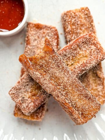 Cinnamon sugar French toast sticks on a cream plate with a dish of syrup.