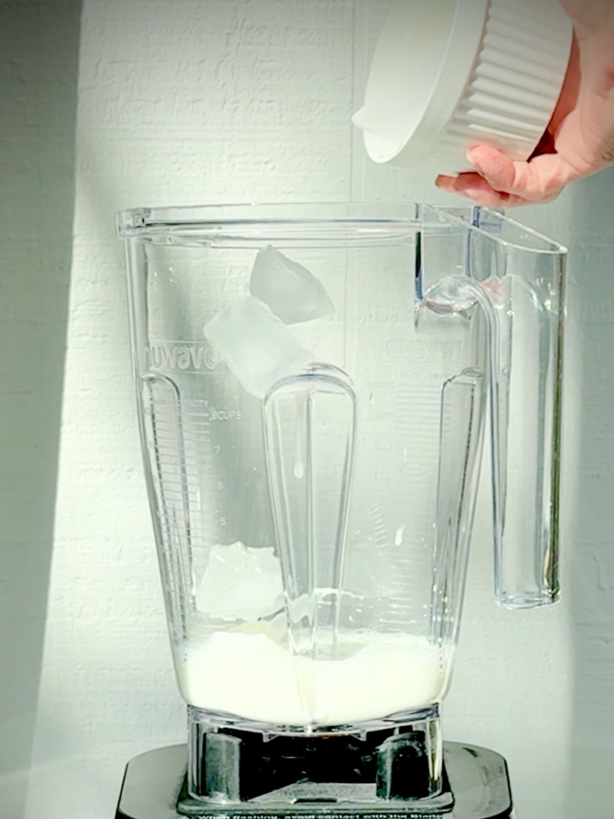 Adding ice to a blender with the ingredients for an avocado banana smoothie.