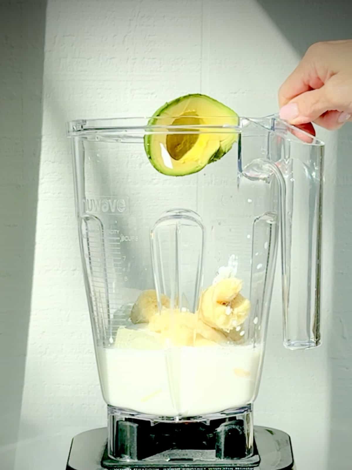 Adding avocado to the ingredients for an avocado banana smoothie.