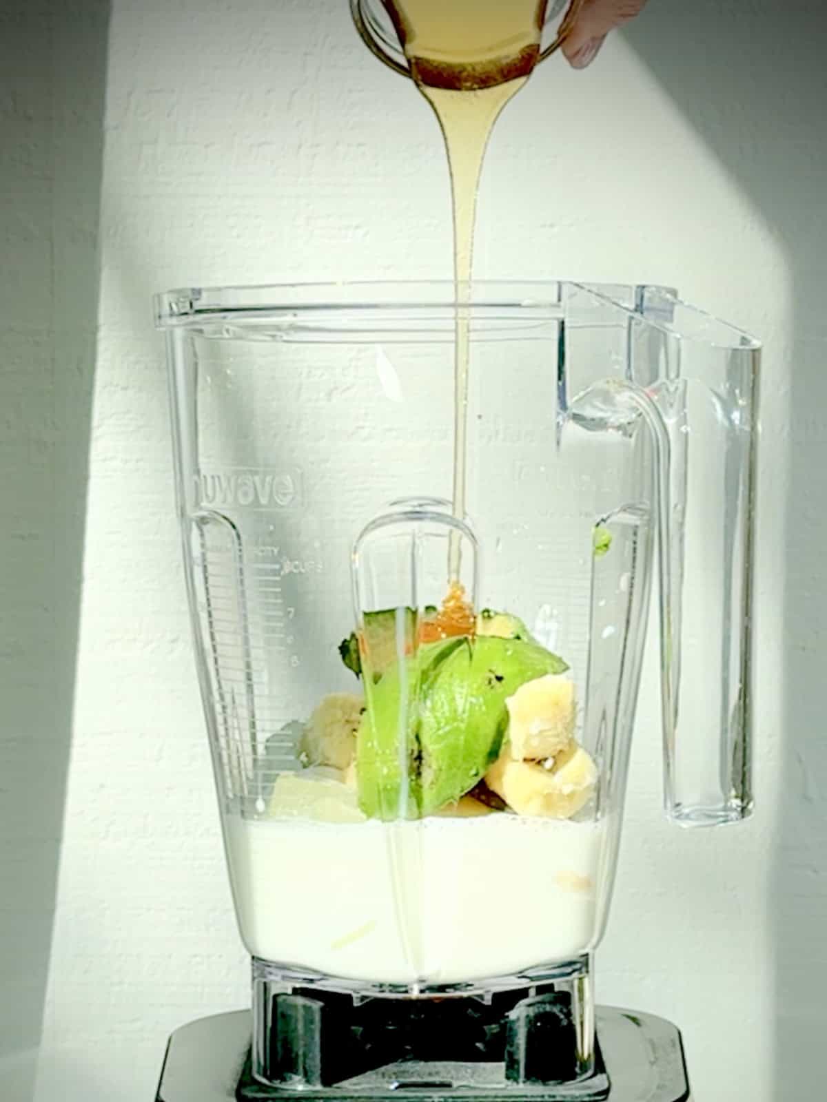 Adding honey for an avocado banana smoothie into a blender.