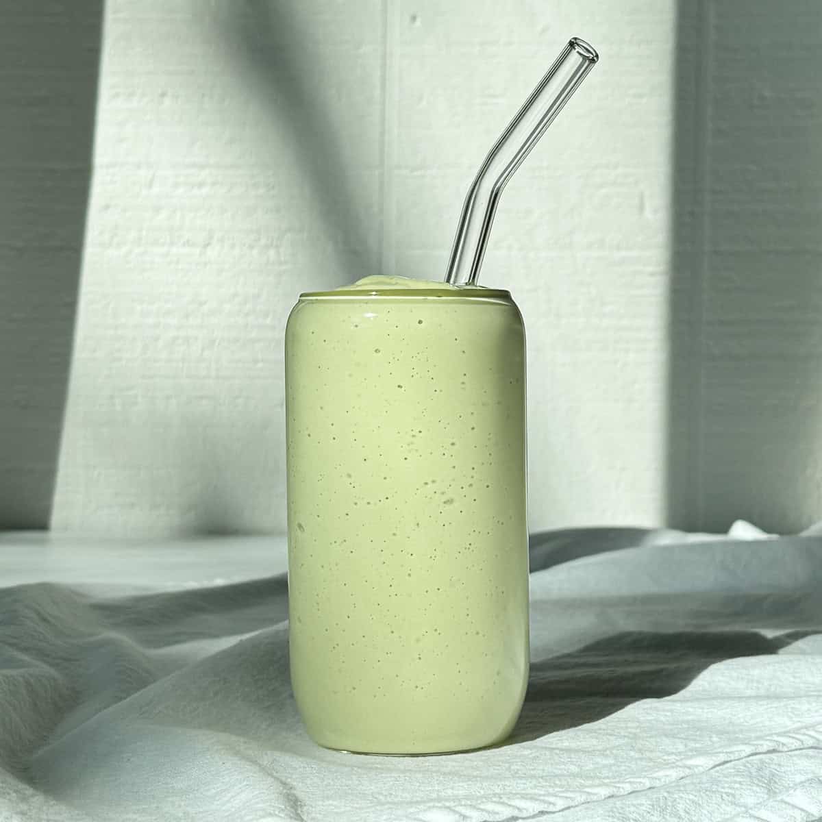 An avocado banana smoothie in a glass with a straw.