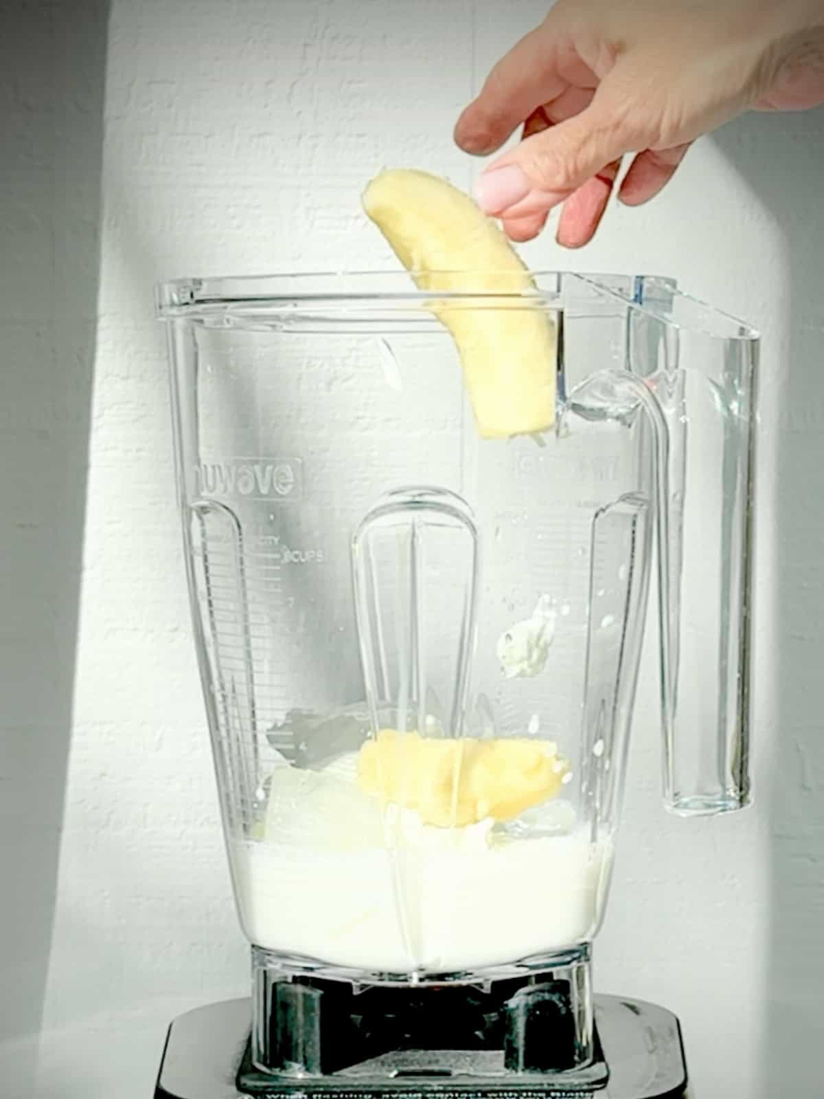 Adding banana to avocado banana smoothie in a blender.