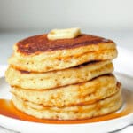 A stack of pancakes with maple syrup on a white plate.