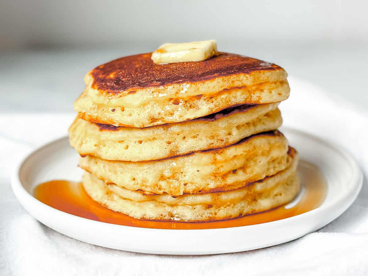 A stack of pancakes with maple syrup on a white plate.