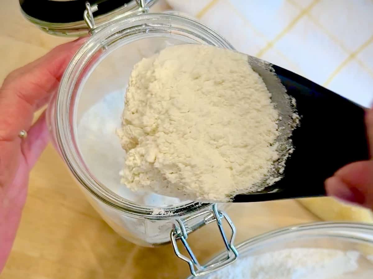Scooping homemade pancake mix into a large airtight container.