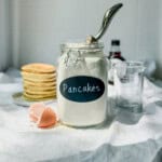 Homemade pancake mix in an airtight container next to a stack of pancakes.
