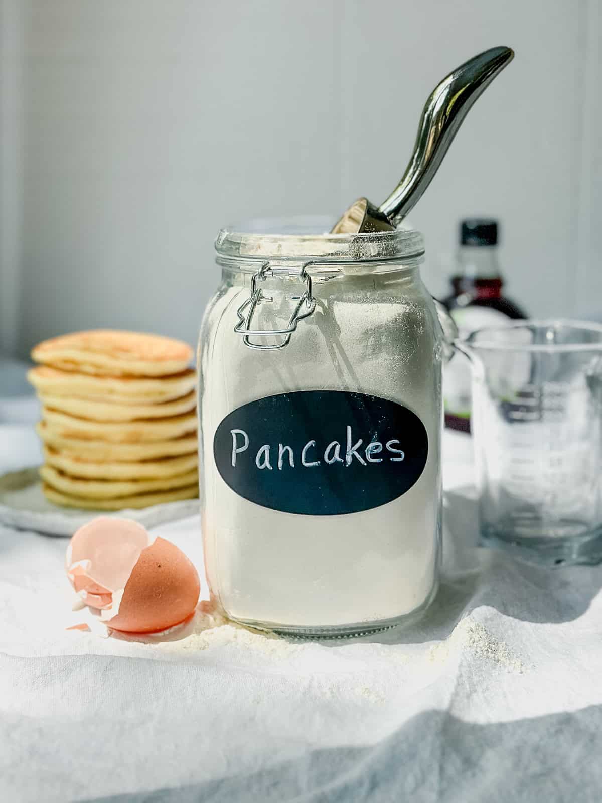 Homemade pancake mix in an airtight container next to a stack of pancakes.