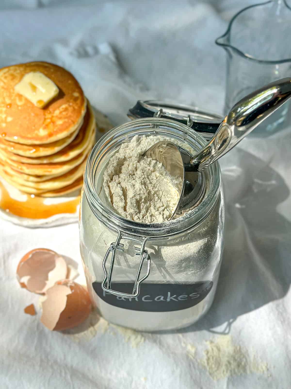 Homemade pancake mix in an airtight container next to a stack of pancakes.