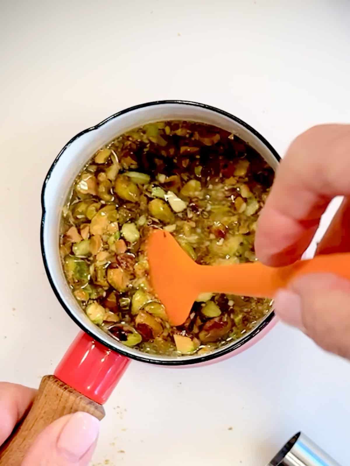 Stirring chopped pistachios into sugar and water to make pistachio syrup.